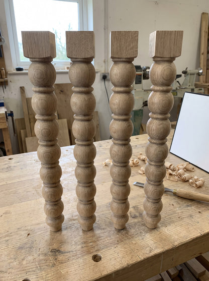 Set of four Milk Street bobbin legs in English oak on the workshop bench, each turned from a single stick with six graduated beads